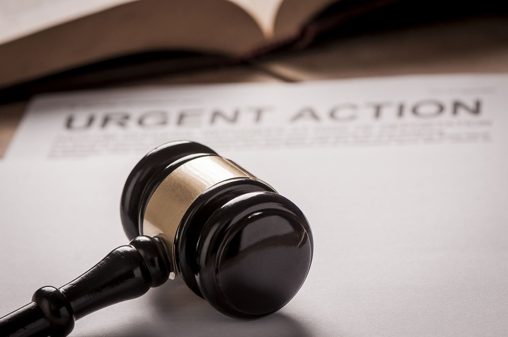 A gavel sitting on a legal notice that reads "urgent action."